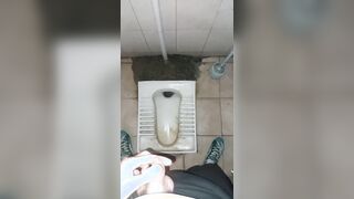 A chav man is urinating in a filthy public restroom