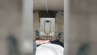 A chav man is urinating in a filthy public restroom