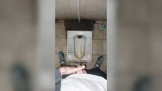 A chav man is urinating in a filthy public restroom