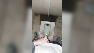 A chav man is urinating in a filthy public restroom